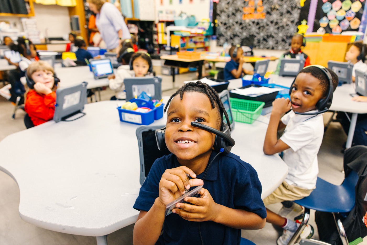 A smiling child wearing headphones beside a tablet in a Liberty County classroom