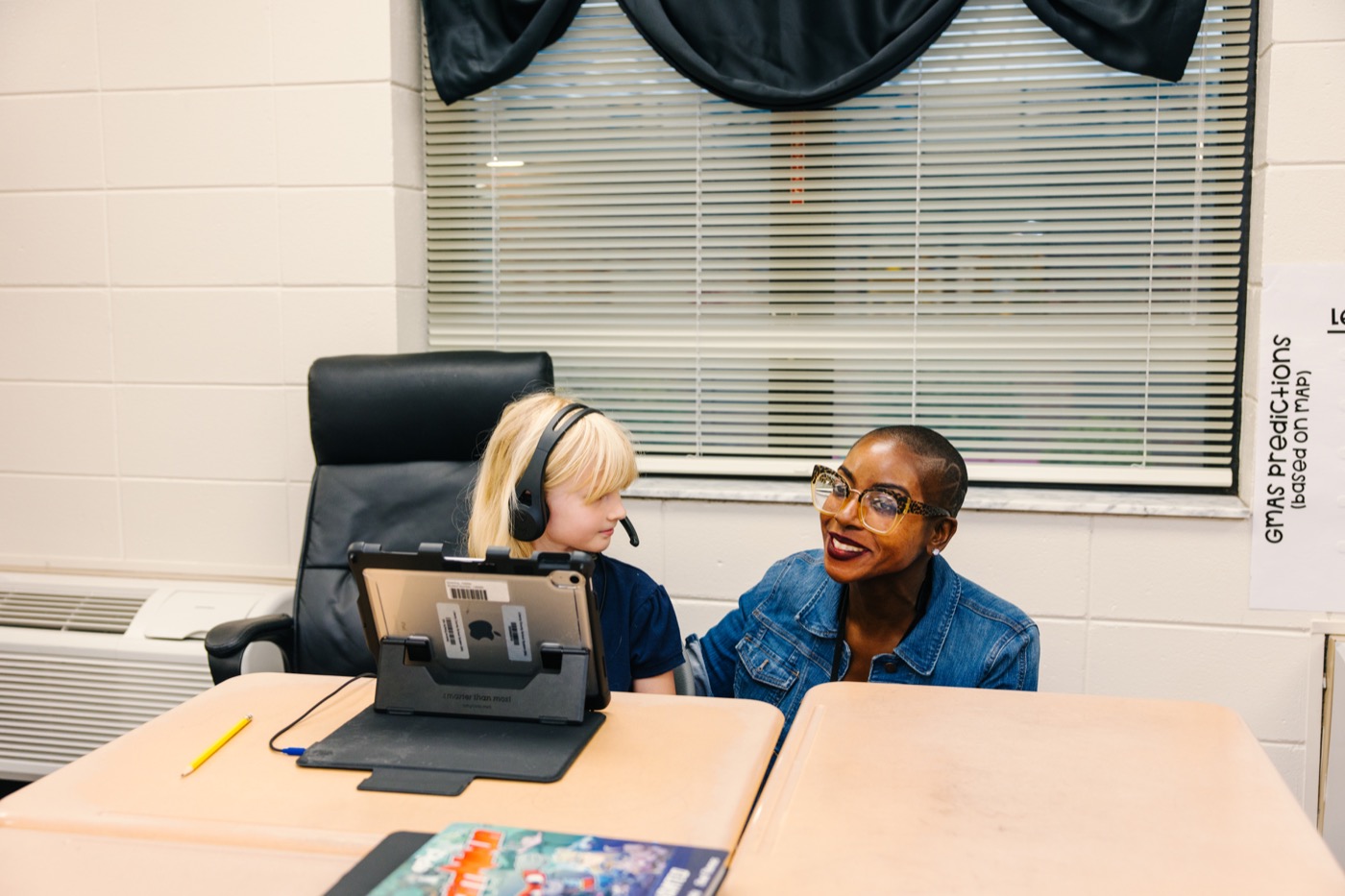 An adult supporting a child beside a classroom tablet